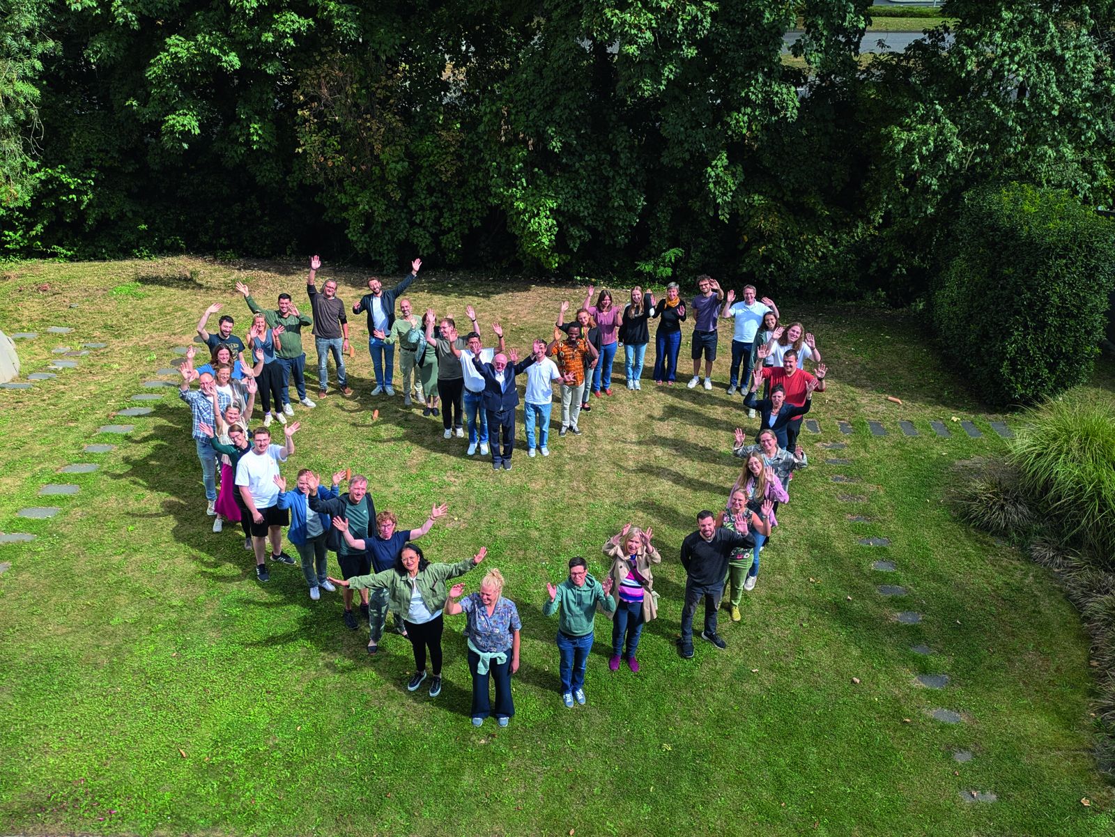 Das Team der Don Bosco Mission Bonn steht auf einer Wiese in Herzform und winkt in die Kamera.